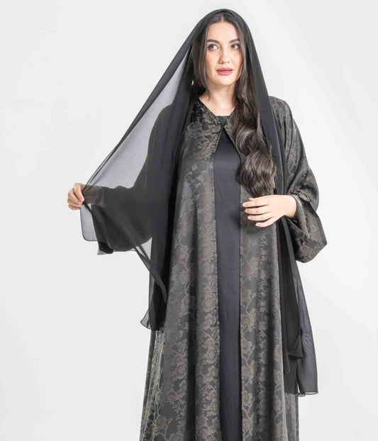Woman wearing a long, dark gray abaya with a black overlay on a white background