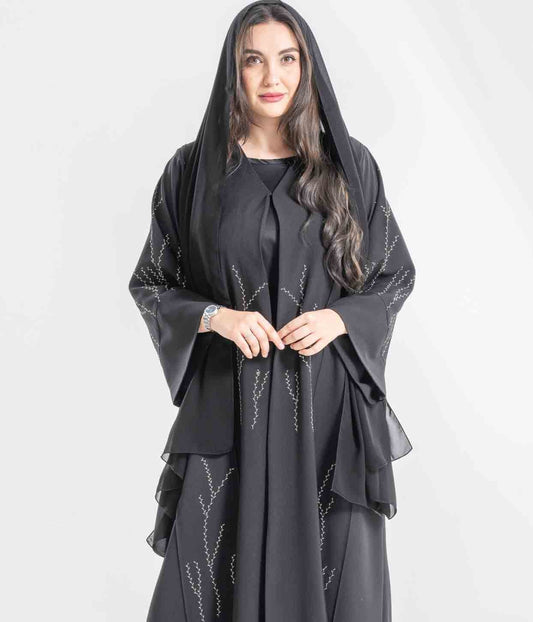 Woman wearing a black abaya with intricate designs on a white background
